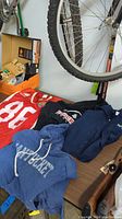 Lot includes one red football shirt with number 88, a black Brockton Boxers football hoodie, a blue Nantucket hoodie, and a navy Patriots hoodie, arranged on a surface with bicycle wheels visible above.