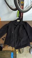 Navy wool pea coat laid flat showing front and loose buttons beside it.
