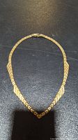 Full view of gold-tone silver necklace laid flat on dark surface showing chain and leaf pattern design