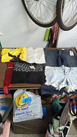 Clothes laid on table showing full assortment including jeans, denim shorts, knit sweater, sleeveless top, yellow and white t-shirts all with tags visible.