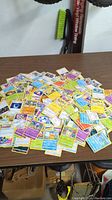 Wide image of a large spread of assorted Pokemon trading cards laid out on a table, showing multiple character and energy cards.