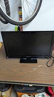 Front view of Sansui 22 inch LED TV sitting on table with bike wheel in background.