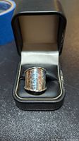 Silver wide band ring with hammered texture inside a black ring box.