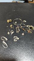 Overview of assorted silver jewelry scrap items laid out on black background showing earrings, rings, pendants and a bangle.