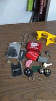 Photo showing the assorted contents of the lot spread out on a wooden surface, including keys, key fobs, a red keychain holder, metal chain, yellow plastic tool, padlock, and plastic clips.