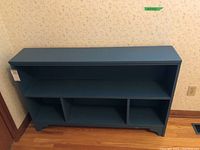 Front view of the blue painted bookcase showing three lower compartments and one upper long shelf.