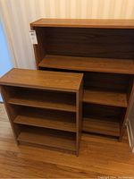 Pair of small bookcases, larger with wood veneer resembling teak, smaller with foil veneer, front angle view.