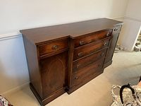Front view showing the solid wood buffet with center dovetail drawers, side cabinet doors with wood inlay, metal oval handles, and a rich dark finish.
