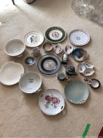 Overview of assorted china laid on carpet including plates, small bowls, creamer and sugar bowl, tea strainer, and serving dishes