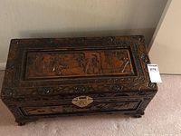 Top angle of rectangular carved wooden storage box showing detailed Chinese scenes carved in relief on the top panel and decorative carved border.