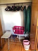 Photo showing assorted hangers, garment bags, pink laundry basket, shoe racks, shower chair, and plastic baskets in a closet.