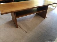 Side angle view of rectangular coffee table showing wood veneer surface, particleboard legs, and lower shelf beneath top.