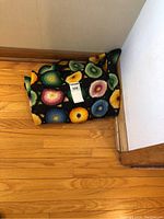 Photo of the folded crochet throw resting on the hardwood floor, showing part of the colorful circular pattern.