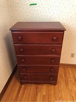 Front view showing five drawers with round wooden knobs, reddish-brown finish, and overall rectangular shape of the dresser.