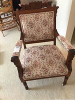 Front view of the Eastlake style antique armchair showing floral upholstery on the seat, backrest, and armrests, carved wood frame, and caster wheels on legs.