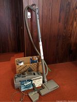 Full setup showing Electrolux canister vacuum with attached hose, power head, extra bags, and manuals on red carpet background.