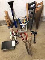 Full assortment of hand tools including axes, saws, hedge shears, brush, trowels, and small hand tools arranged on the ground.