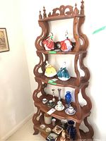 Five tier wooden display shelf holding various knick knacks, photographed from front left corner showing full height and detail of shelves.