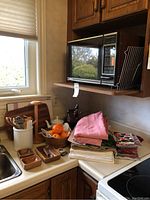 Shows black Quasar microwave on wooden shelf above counter with utensil rack beside it. Counter holds wooden bowls, linens, and placemats.