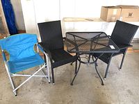 Photo showing all four items: black metal mesh patio table, two black plastic wicker outdoor chairs, blue folding camp chair with white frame.