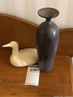 Photo showing signed pottery vase and white ceramic loon figurine side by side on wooden surface.