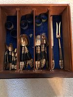 Brass cutlery set with spoons, forks, carving knife, and fork arranged in a wooden tray lined with blue felt.