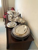 Wide view of assorted silver plate items including tea and coffee pots, creamers, sugar bowl, candlesticks, butter dish, and various trays.