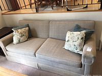 Full view of light brown tweed style sofa with floral and solid green throw pillows.