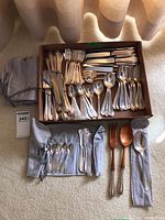 Wide shot of assorted sterling silver flatware in box and cloth pouches on carpet