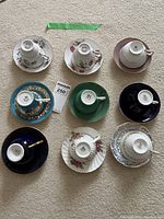 Nine assorted teacup and saucer sets arranged in a grid on carpet