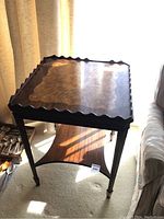 Front angle showing the entire antique wooden tiered table with scalloped edges, dark wood finish, and shadowing on carpet.