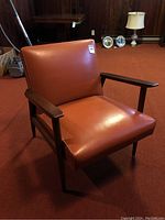 Side view of vintage burnt orange mid century occasional chair showing wooden armrests and upholstery.