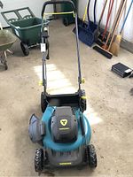 Front view of Yardworks electric mower showing the handle, body, wheels, and side chute for grass collection in a garage environment.