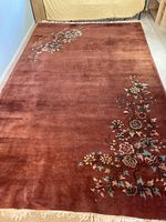 Full view of the burgundy area rug laid flat showing floral pattern mainly on two corners and the fringe edge.
