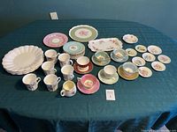Full display of assorted china pieces on green tablecloth showing teacups, saucers, plates, and trays with floral designs.