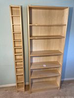 Photo showing both the wider bookshelf with five shelves and the narrow CD/art shelf with small compartments, both in light wood.