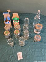 Photo showing multiple clear glass canning jars and two swing top jars along with a swing top glass bottle.