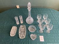 Full lot arrangement showing crystal decanter in center surrounded by six wine glasses, two tall glasses, and four crystal dishes and bowls arranged on green tablecloth.