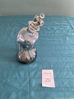 Front view of the clear glass decanter with melting appearance and round stopper in place on a blue cloth background.