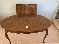 View of oval wooden dining table top showing detailed wood grain finish with chairs behind.