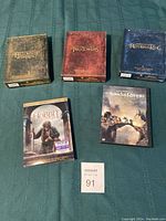 Three box sets and two individual DVDs from the Lord of the Rings collection and The Hobbit laid out on a green fabric background with auction tag.
