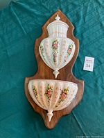 Front view of the Italian ceramic wall fountain showing floral painted vessels with wooden backing.