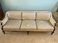 Full front view of the light coloured floral chesterfield sofa showing three seat cushions and wooden base and legs.