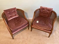 Pair of caned-back tub chairs with burgundy upholstery cushions, shown side by side on carpet.