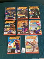 Nine Nintendo Power issues laid out on tabletop including Super Castlevania II, The Manhattan Project, WWF WrestleMania, Magical Tetris Challenge, Let’s A-Game, Mario Paint and Street Fighter II Turbo covers