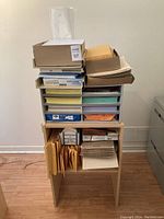Full view of wooden shelf with various paper supplies including boxes and stacks of envelopes, folders, and mailers.