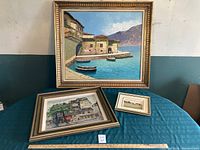 Three framed paintings shown together on a table, largest at back, two smaller in front.