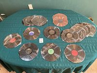 Seventeen 10-inch vinyl records arranged on a green cloth table, some stacked and all wrapped in clear cellophane, showing various labels and no jackets.