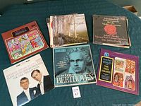 Six classical music vinyl records laid out on a bed.