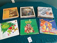 Six vinyl records on a blue tablecloth including Foggy Mountain Banjo by Flatt & Scruggs, Sesame Street, Hogg Family Bluegrass, Dr. Seuss How the Grinch Stole Christmas, The Banana Splits, and a Star Wars record.